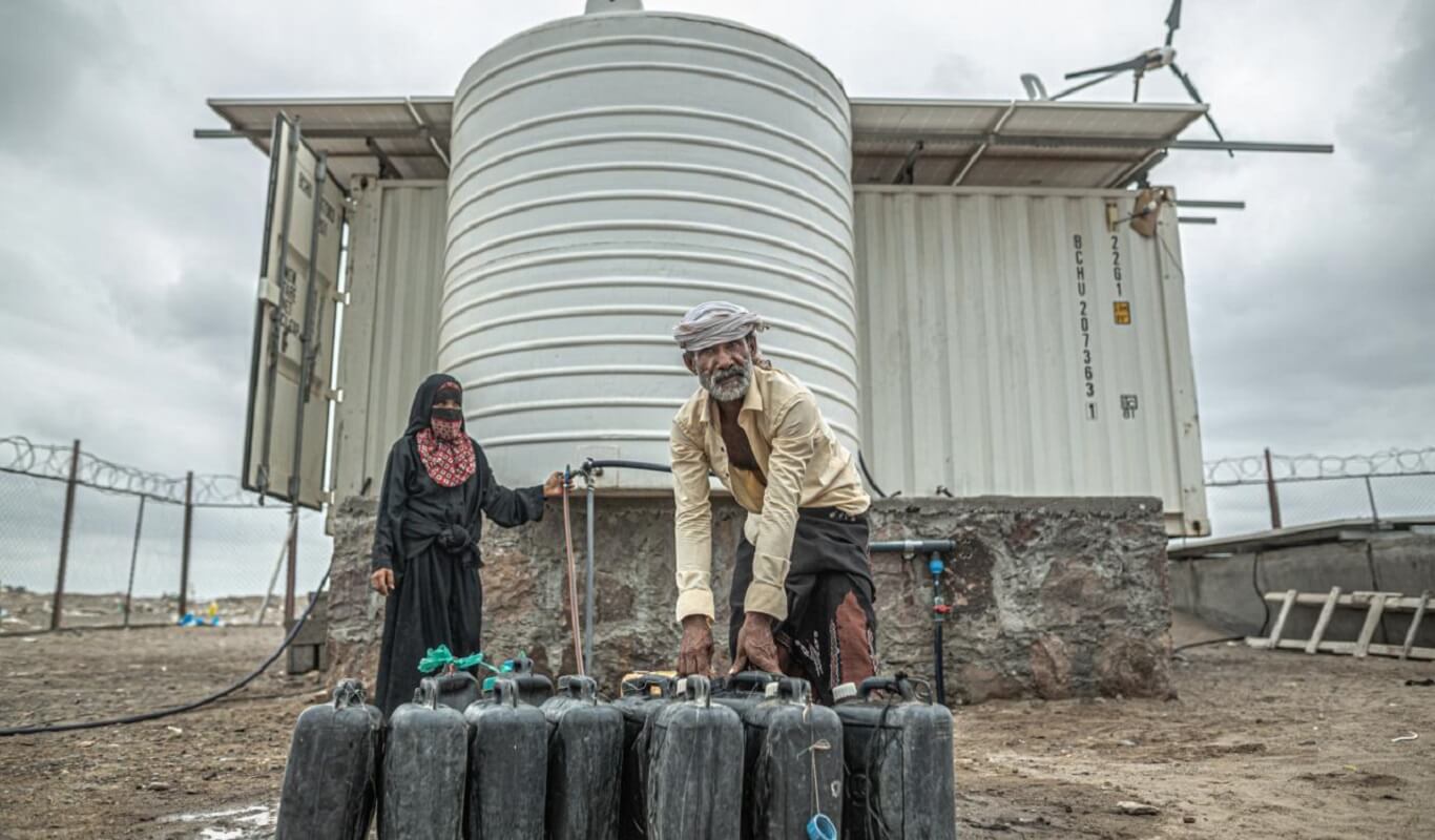 A Yemeni man and woman fill up several water cans from a water desalination facility.
